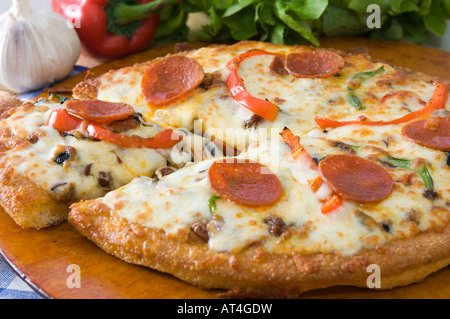 A hot mozzarella & pepperoni Pizza pie presented with fresh produce on a wooden platter Stock Photo