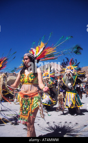 Beautiful girl wearing colourful feather headdress leading masked tobas dancers at the Ch'utillos festival, Cerro Rico in background, Potosi, Bolivia Stock Photo