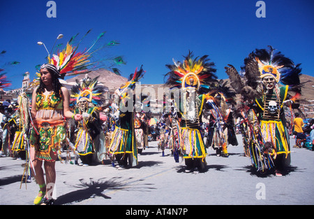 Beautiful girl wearing colourful feather headdress leading masked tobas dancers at the Ch'utillos festival, Cerro Rico in background, Potosi, Bolivia Stock Photo