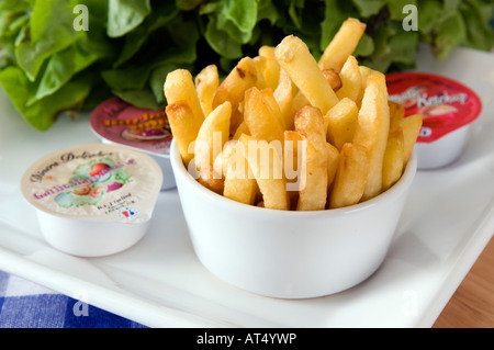 A bowl of golden french fries displayed with a range of packaged dips Stock Photo