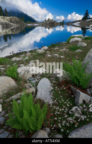 Lake Ann reflecting clouds in the glacial hanging valley above the distant peaks of the North Cascades in Washington state Stock Photo