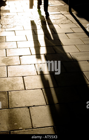 dramatic shadows of people shopping walking on pavement sidewalk Stock Photo