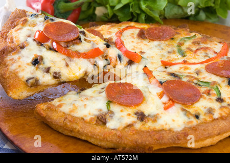 A hot mozzarella & pepperoni Pizza pie presented with fresh produce on a wooden platter Stock Photo