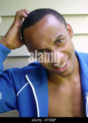 Lifestyle Portrait of a Handsome Man of African Ethnicity He is Wearing an Unzipped Blue Jacket and is Scratching His Head Stock Photo