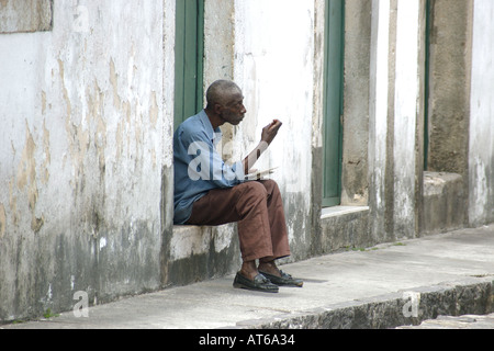 An introspective old man sits down at sidewalk on the streets of Pelourinho world heritage site in Salvador Bahia Brazil Stock Photo
