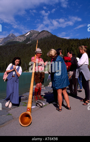 Alphorn Blower with Alpenhorn talking to Tourists at Lake Louise, Banff National Park, Canadian Rockies, Alberta, Canada Stock Photo