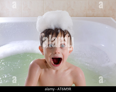 Child with funny surprised look in Tub with bubbles on head. Bubble bath.