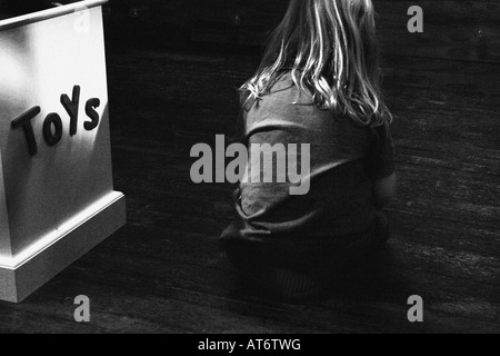 Young boy sits on the floor next to a toy box Stock Photo