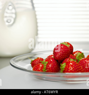 Strawberries on glass plate in front of milk jar, close-up