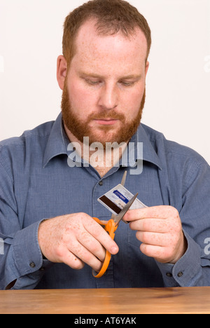 young man cutting up credit debit bank card with scissors Stock Photo