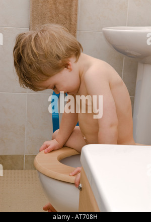 male toddler sitting on toilet looking down between legs into pan Stock Photo