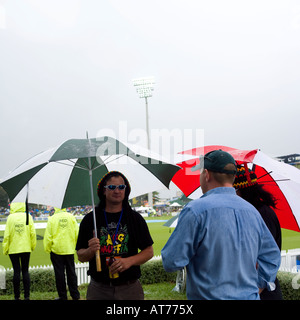 Dressed up Jamican style fans under umbrella at cricket ground drinking beer whiles its raining Stock Photo