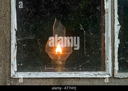 old oil lamp with broken glass burning at window of a timber wooden house Stock Photo