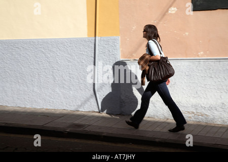hispanic spanish woman walking at speed up a street with shadow on the wall tenerife canary islands spain Stock Photo