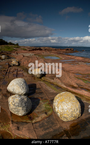 granite erratics boulders on sandstone bedrock on the shore at pirates cove near Corrie on the Isle of Arran in summer Stock Photo