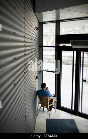 body guard indoors sitting on a chair in front of a wide window with a metallic screen in the left side Stock Photo