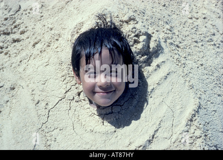 Young local boy is buried in sand up to his neck. Stock Photo