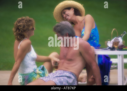 Friends talk and relax poolside with drinks and food. Stock Photo