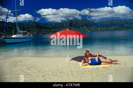 A mother and daughter relax under a red umbrella on a sandbar at Kaneohe bay on the windward side of Oahu. Stock Photo
