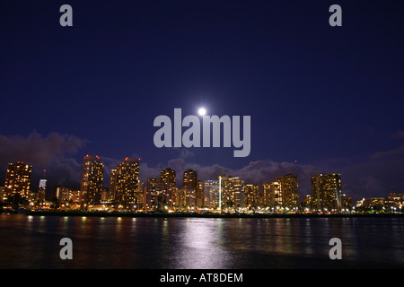 The city lights of Honolulu glow bright as a full-moon rises from behind. Stock Photo