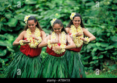 Three Hula Dancers in ti leaf skirts and yellow plumeria leis performing an Auana style hula Stock Photo