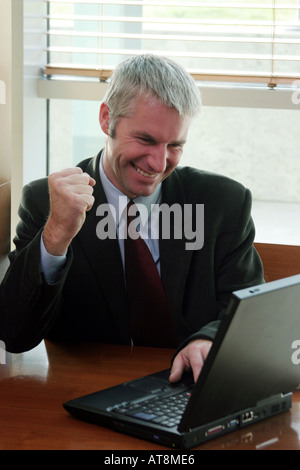Businessman in front of notebook computer clenching his fist at clinching the deal. Stock Photo