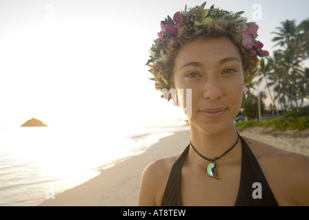 A beautiful young woman wearing a haku lei (floral headpiece) smiles at Lanikai beach on the windward side of Oahu. Stock Photo