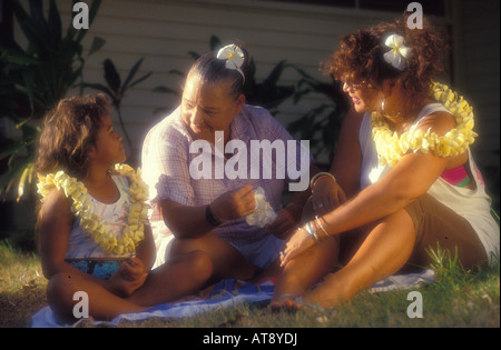 Local polynesian family relaxing out on the lawn in the sun and wearing leis Stock Photo