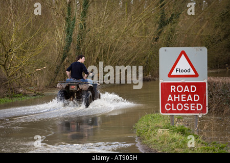 Two lads on a quad bike tackling the B4213 while it was closed due to flooding near Apperley, Gloucestershire in March 2007 Stock Photo