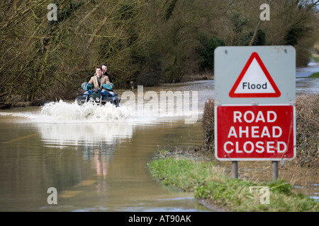 Two lads on a quad bike tackling the B4213 while it was closed due to flooding near Apperley, Gloucestershire UK in March 2007 Stock Photo