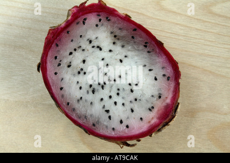 Half a white fleshed dragon fruit. Small black seeds in white flesh on light wood background. Stock Photo