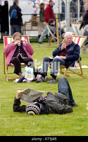 Young man reading newspaper lying on grass in front of people in deckchairs at The Guardian Hay Festival 2007 Powys Wales UK EU Stock Photo