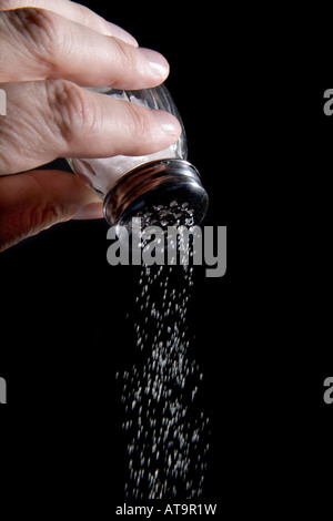 Hand holding Salt shaker with salt coming out Stock Photo