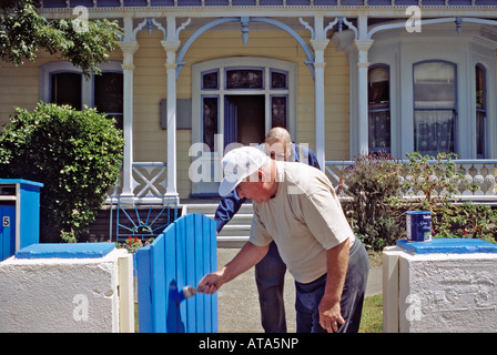 Man painting gate as another man looks on in a residential area of Wellington New Zealand Stock Photo