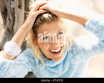 Portrait of pretty young blond woman sitting on beach in Maui Hawaii smiling and holding back hair with hands Stock Photo