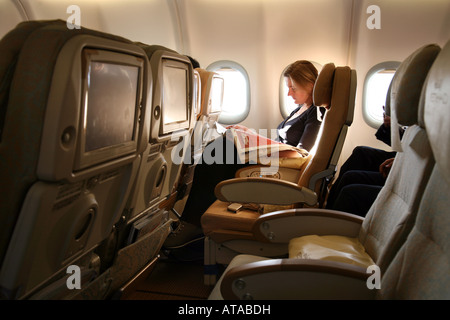 A woman female air passenger reading in the cabin with empty seats on a plane flight; Etihad airline Stock Photo