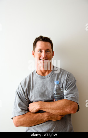 Head and shoulder portrait of man in t shirt against white wall holding water bottle and smiling Stock Photo