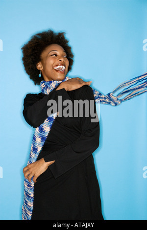 Half length studio portrait of smiling happy woman flinging scarf over shoulder on blue background Stock Photo