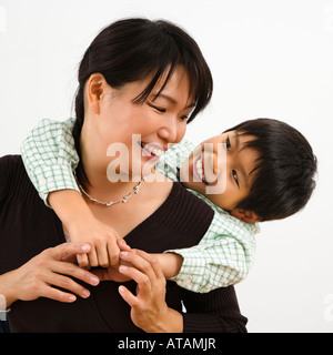 Asian mother with young son hugging her from behind smiling Stock Photo