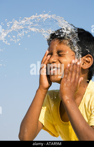 Indian boy splashing water on his face against a blue sky. India Stock Photo