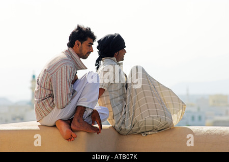 Two young men sitting on wall overlooking town in Oman Stock Photo
