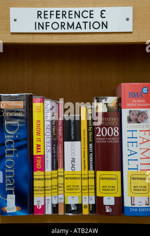 Row of reference books on shelf in public library & sign (close up of dictionary, almanack & non-fiction reading material) - Yorkshire, England, UK. Stock Photo
