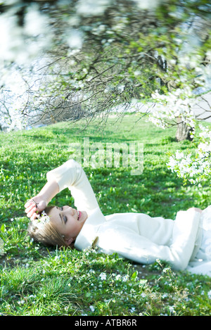 Teenage girl lying on the ground with eyes closed, holding flower, smiling Stock Photo