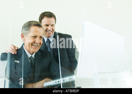 Businessman looking over colleague's shoulder at laptop computer, both smiling, low angle view Stock Photo