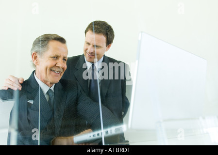 Two businessmen smiling together, one looking down at laptop computer Stock Photo