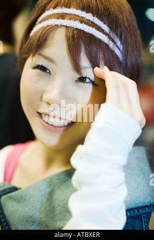 Young woman smiling, touching head, close-up Stock Photo