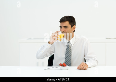 Businessman sitting at table, drinking orange juice, looking away