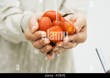 Woman washing handful of tomatoes under faucet, cropped view of hands, close-up Stock Photo