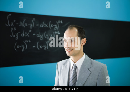Man in suit looking away, smiling, mathematic equation on blackboard in background Stock Photo