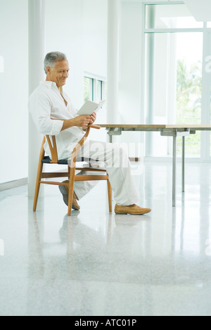Mature man sitting at table, reading book, side view Stock Photo
